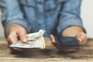 Woman holds dollars and phone in her hands. Online money transfer